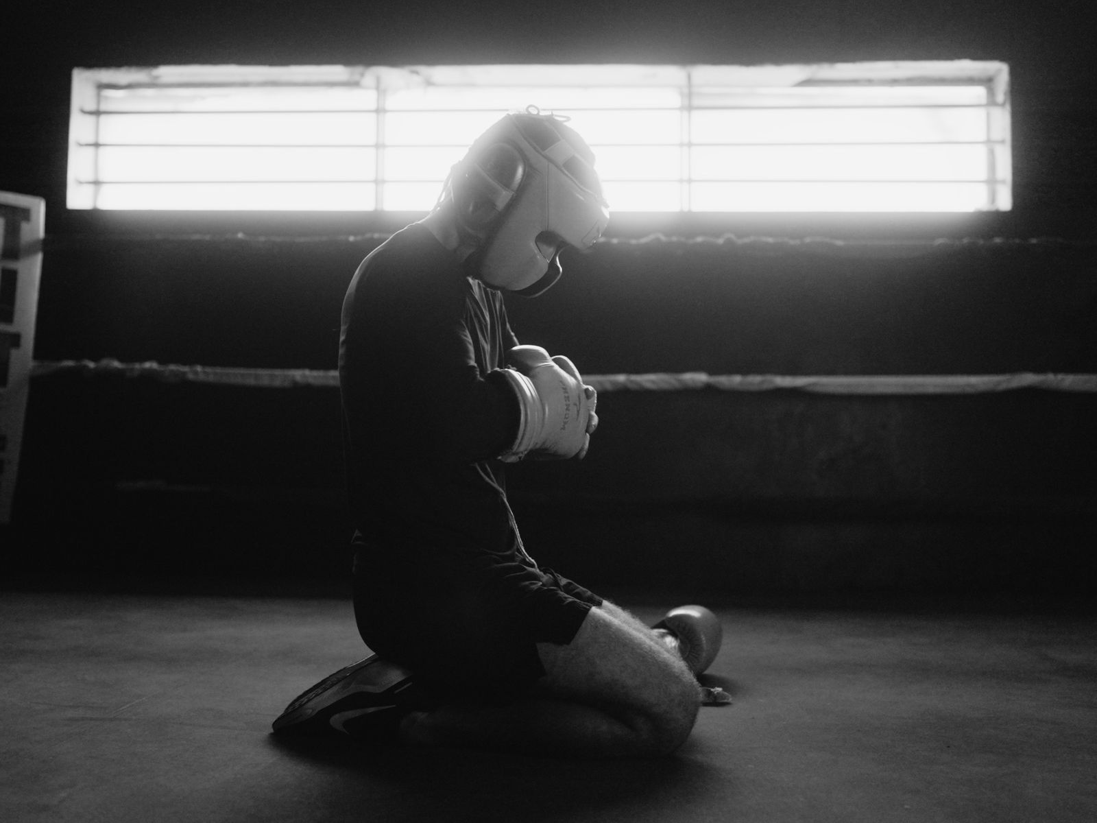 A fighter kneels in the ring in black and white